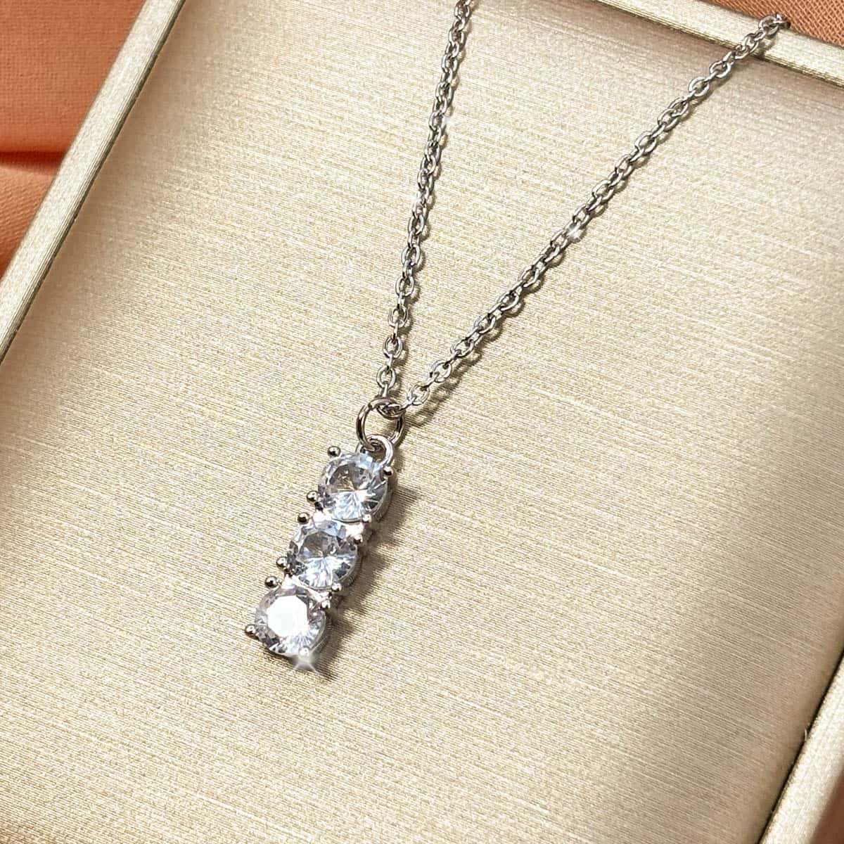 Schlichte silberfarbene Kette mit vertikalem Stab-Anhänger aus drei runden Zirkonia-Steinen, Detail-Aufnahme von links