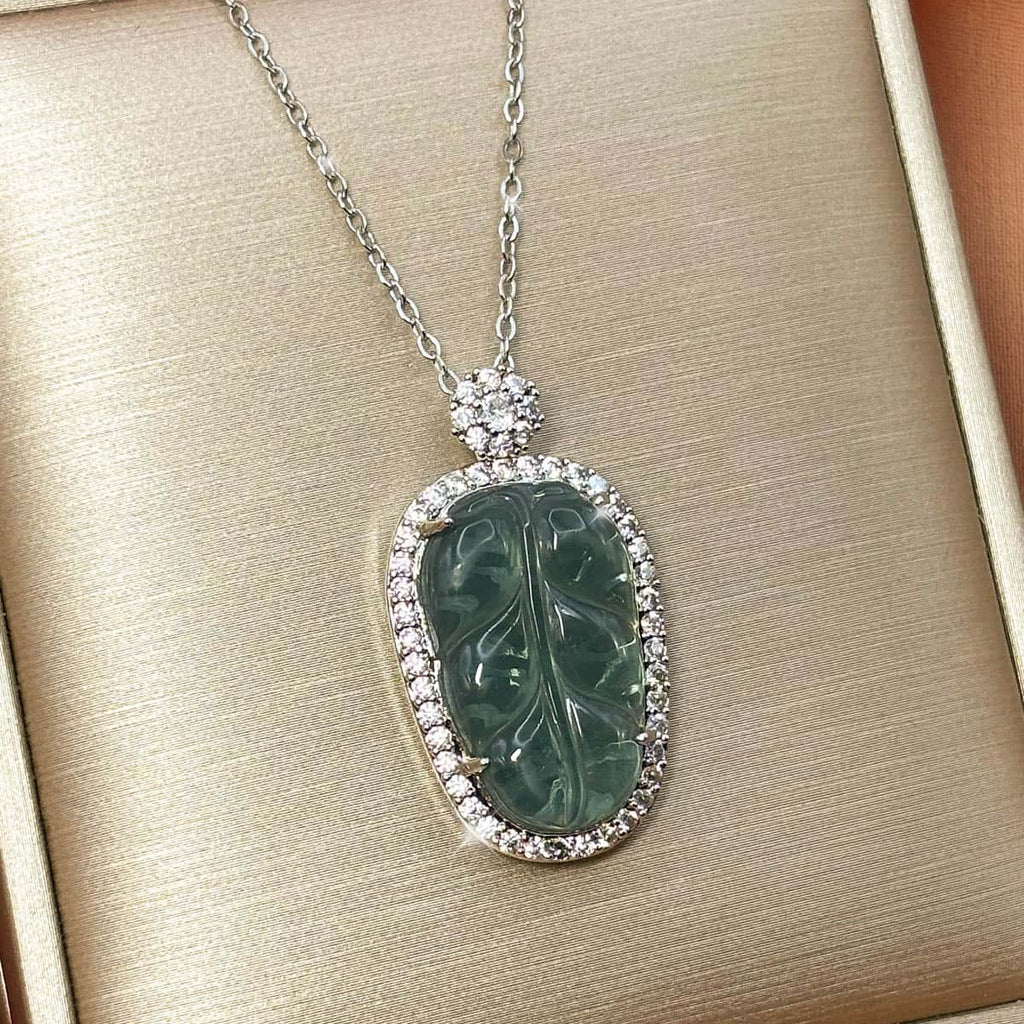 Silberfarbene Kette mit ovalem, grünem Blatt-Anhänger und glitzerndem Zirkonia-Rahmen, Produktfoto von rechts.