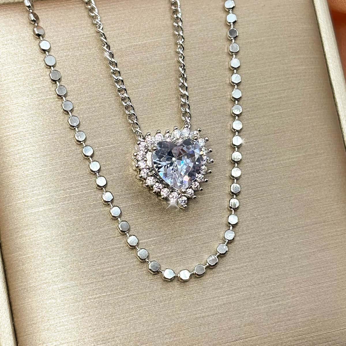 Silberfarbene Halskette mit einem großen Zirkonia-Stein in Herzform und einer Layering Kette, Produktfoto von rechts.