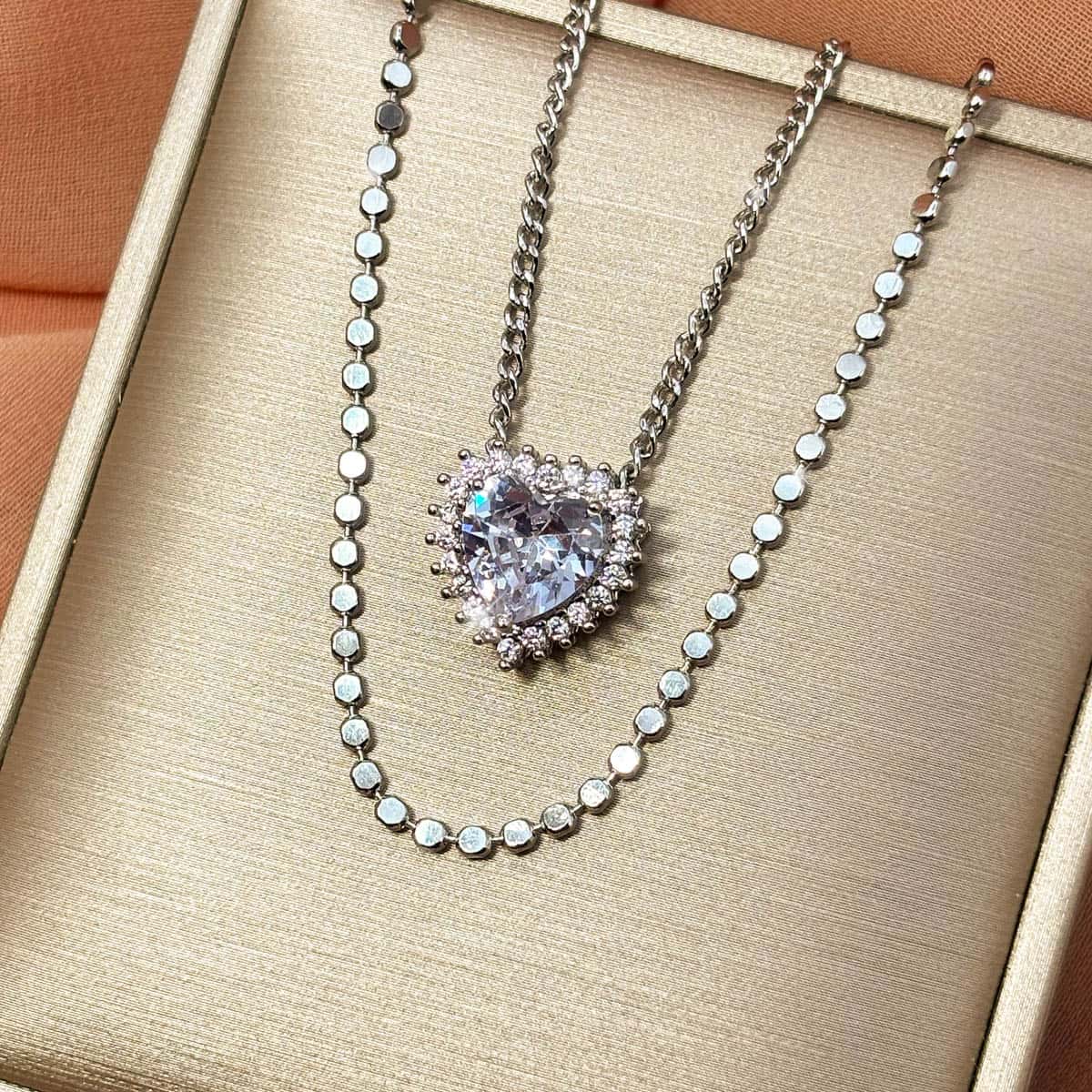 Silberfarbene Halskette mit einem großen Zirkonia-Stein in Herzform und einer Layering Kette, Produktfoto von links