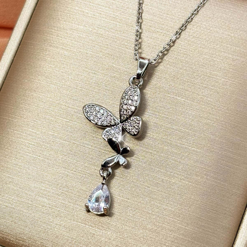 Silberfarbene Halskette mit zwei filigranen Schmetterlingen und einem hängenden Zirkonia-Stein im Tropfen-Schliff, Produktfoto von rechts.