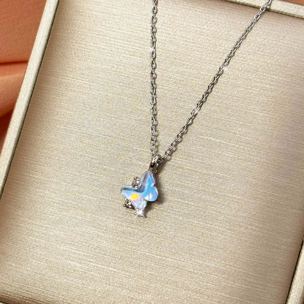 Silberfarbene Halskette mit einem Schmetterlings-Anhänger in hellblau schimmernder Opal-Optik und Zirkonia-Besatz, Produktfoto von rechts.