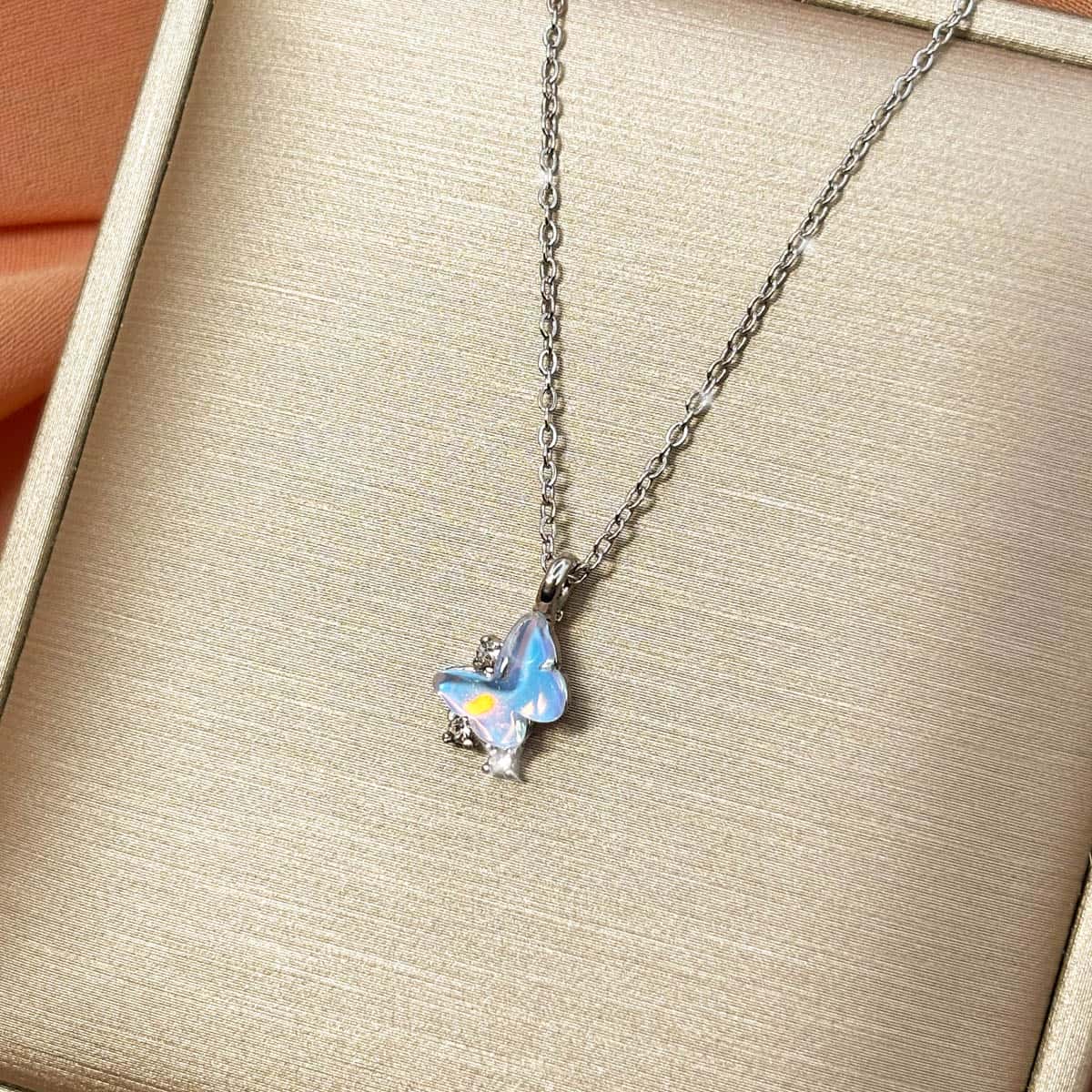 Silberfarbene Halskette mit einem Schmetterlings-Anhänger in hellblau schimmernder Opal-Optik und Zirkonia-Besatz, Produktfoto von rechts.