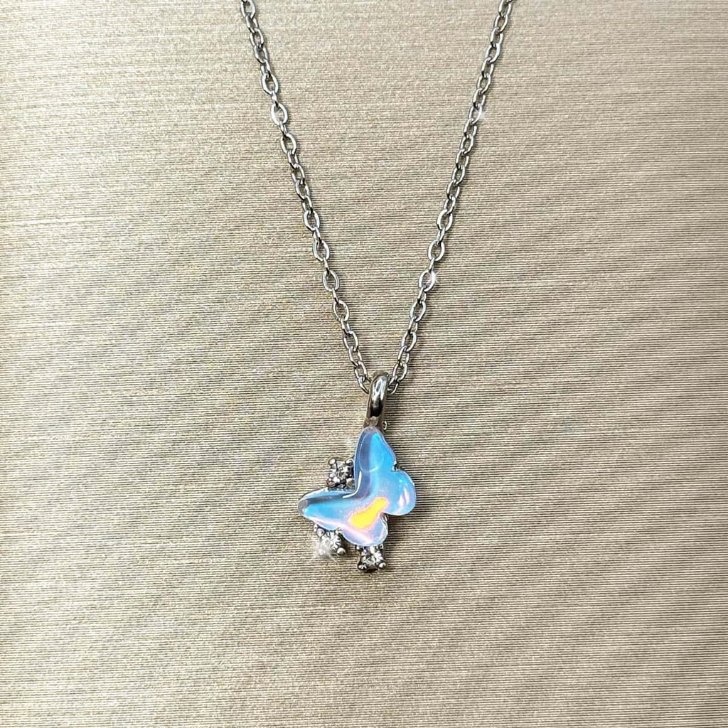 Silberfarbene Halskette mit einem Schmetterlings-Anhänger in hellblau schimmernder Opal-Optik und Zirkonia-Besatz, Produktfoto.