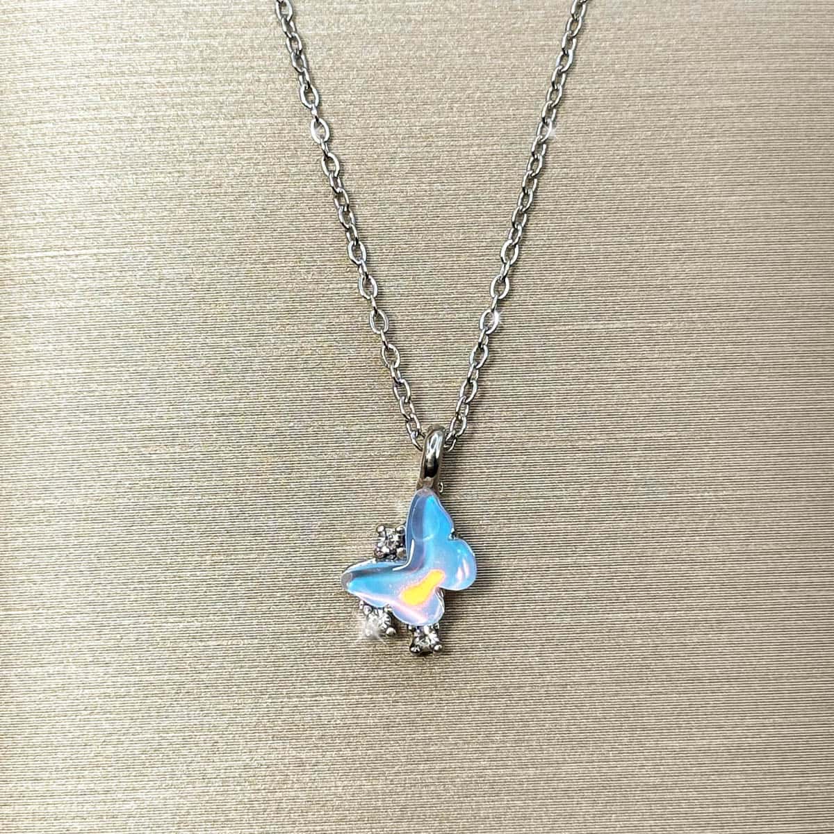 Silberfarbene Halskette mit einem Schmetterlings-Anhänger in hellblau schimmernder Opal-Optik und Zirkonia-Besatz, Produktfoto.