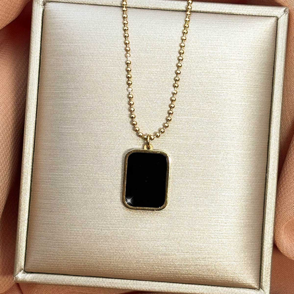 Goldfarbene Damen-Halskette aus Edelstahl mit einem rechteckigen Anhänger in glänzender, schwarzer Onyx-Optik, Produktfoto.