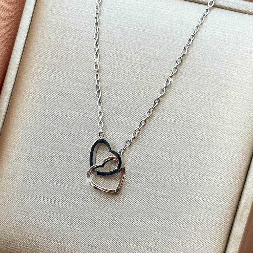 Silberfarbene Damen-Halskette aus Edelstahl mit zwei elegant ineinander verschlungenen Herz-Anhängern, Nahaufnahme.