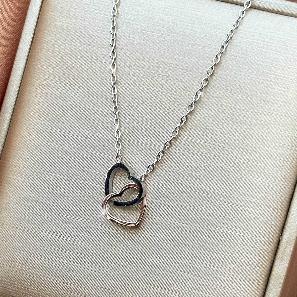 Silberfarbene Damen-Halskette aus Edelstahl mit zwei elegant ineinander verschlungenen Herz-Anhängern, Nahaufnahme.