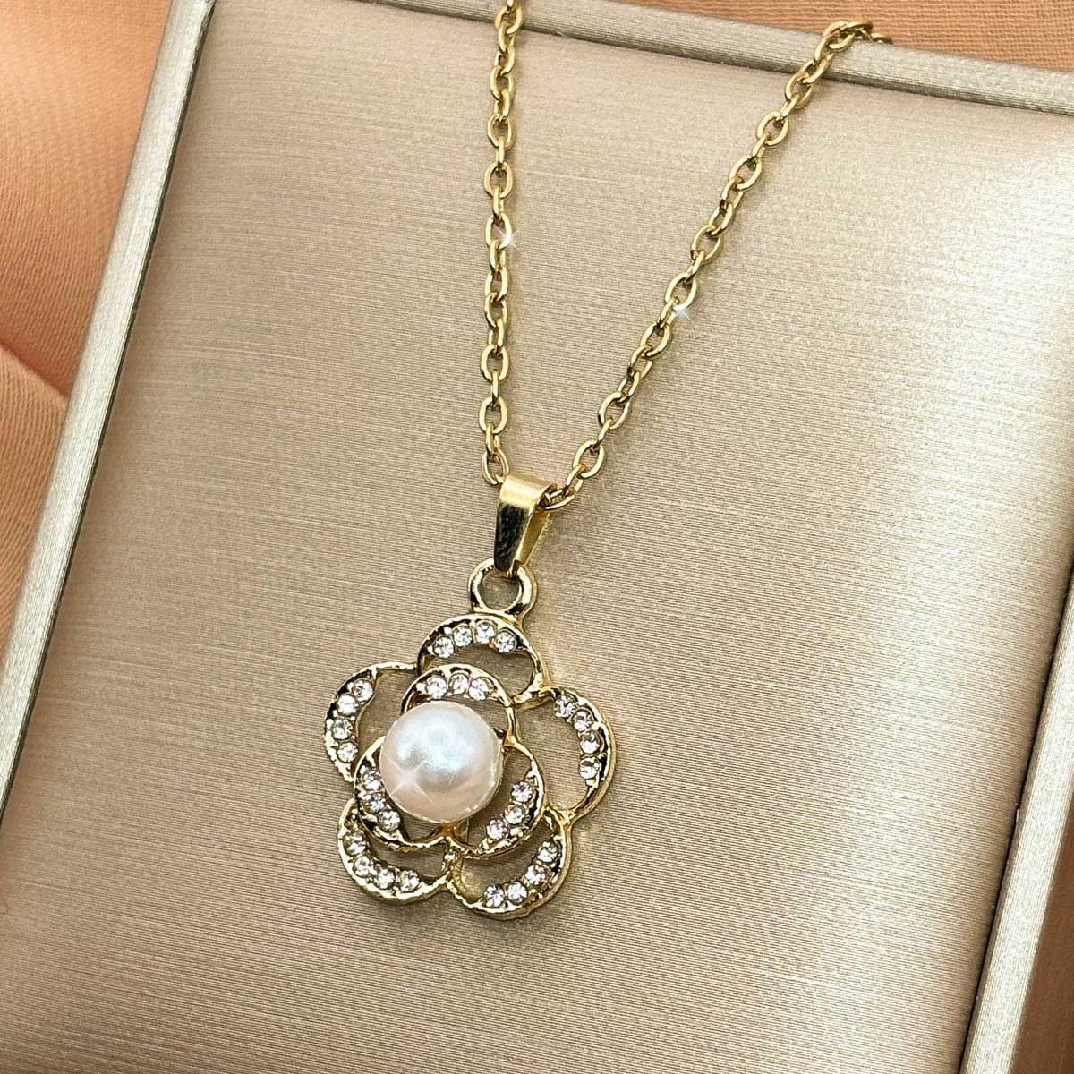 Goldfarbene Edelstahl-Halskette für Damen mit einem zarten Blüten-Anhänger, verziert mit Zirkonia-Elementen und einer weißen Perle, Studioaufnahme.