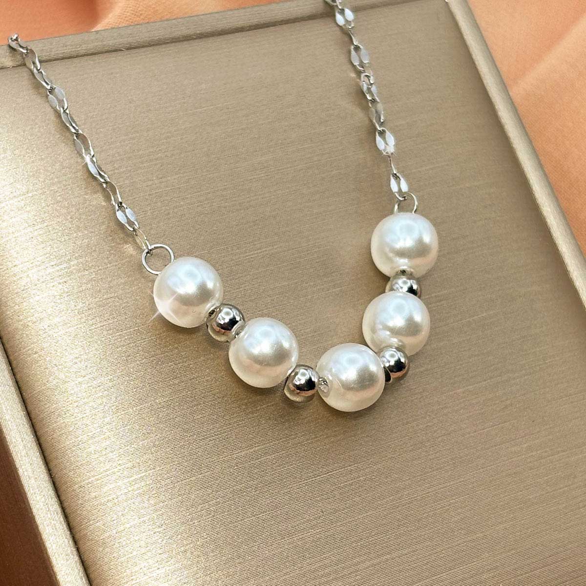 Silberfarbene Edelstahl-Halskette für Damen mit fünf elegant angeordneten, weißen Perlen und kleinen Metallkugeln, Produktbild.