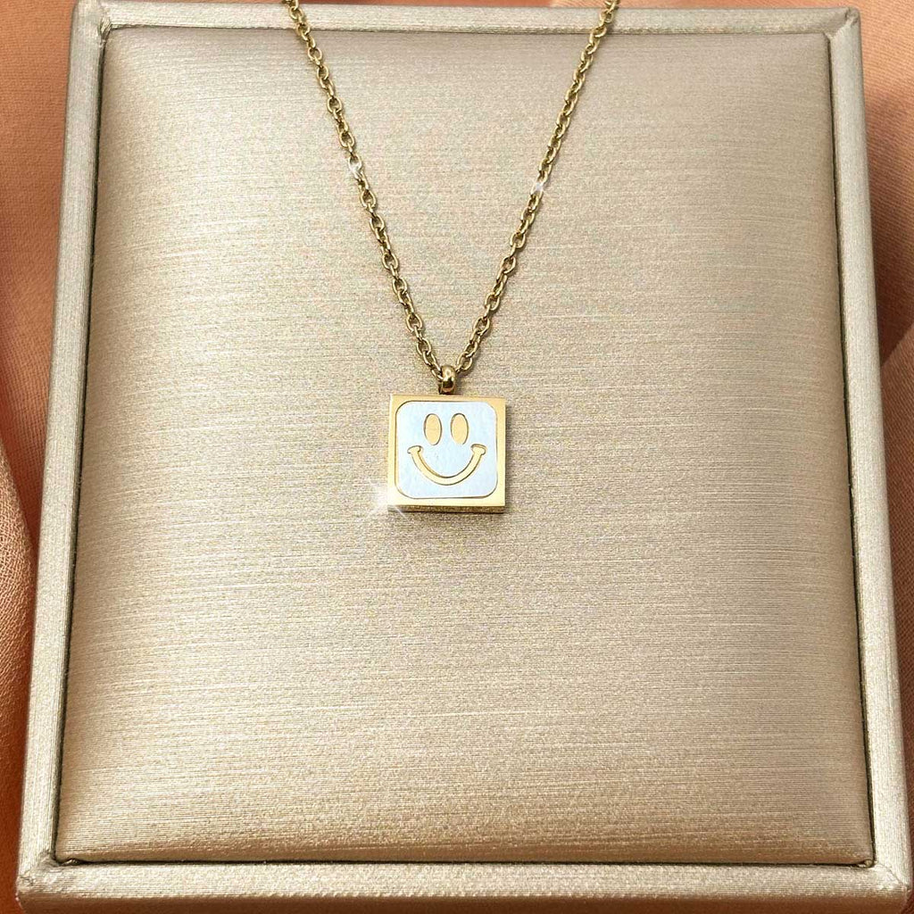 Goldfarbene Edelstahl-Halskette für Damen mit einem quadratischen Anhänger samt hell hinterlegtem, lächelndem Smiley-Gesicht, Produktfoto