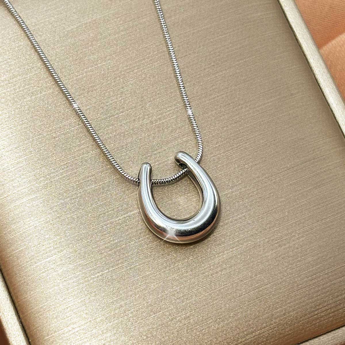 Silberfarbene Damen-Halskette aus Edelstahl mit einem schlichten, glänzenden Hufeisen-Anhänger als Glücksbringer, Produktfoto