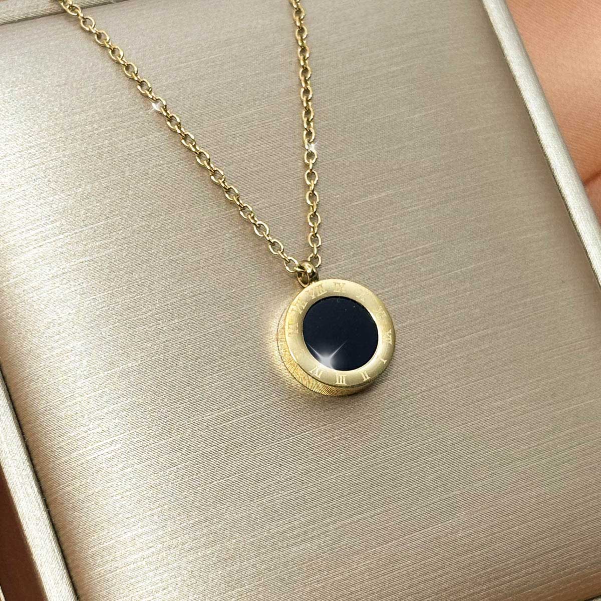 Goldfarbene Damen-Halskette aus Edelstahl mit einem runden Anhänger in schwarzer Onyx-Optik und gravierten römischen Ziffern, Vorderansicht.