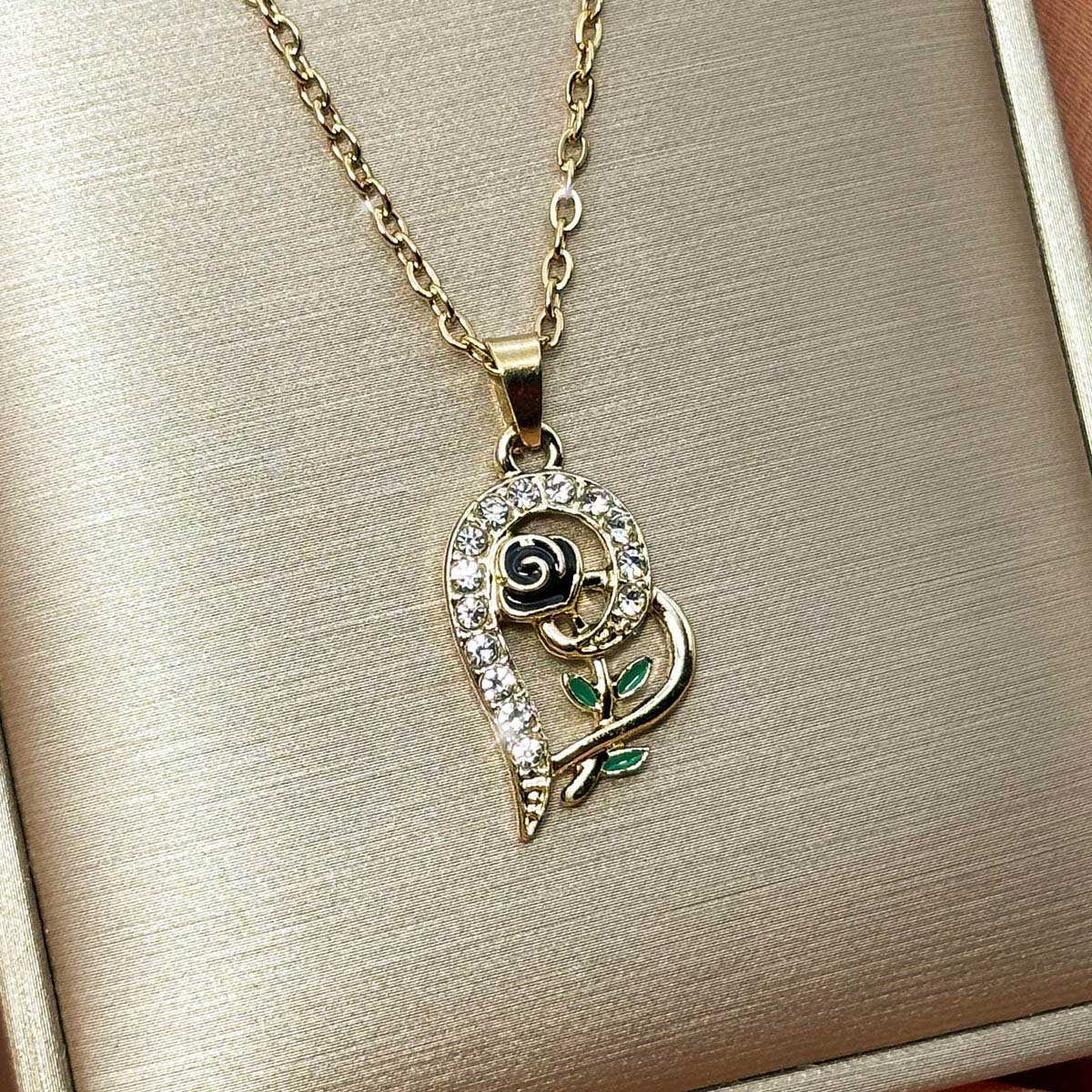 Goldfarbene Damen-Halskette aus Edelstahl mit einem geschwungenen Herz-Anhänger, verziert mit einer kleinen Rose und Zirkonia, Nahaufnahme.
