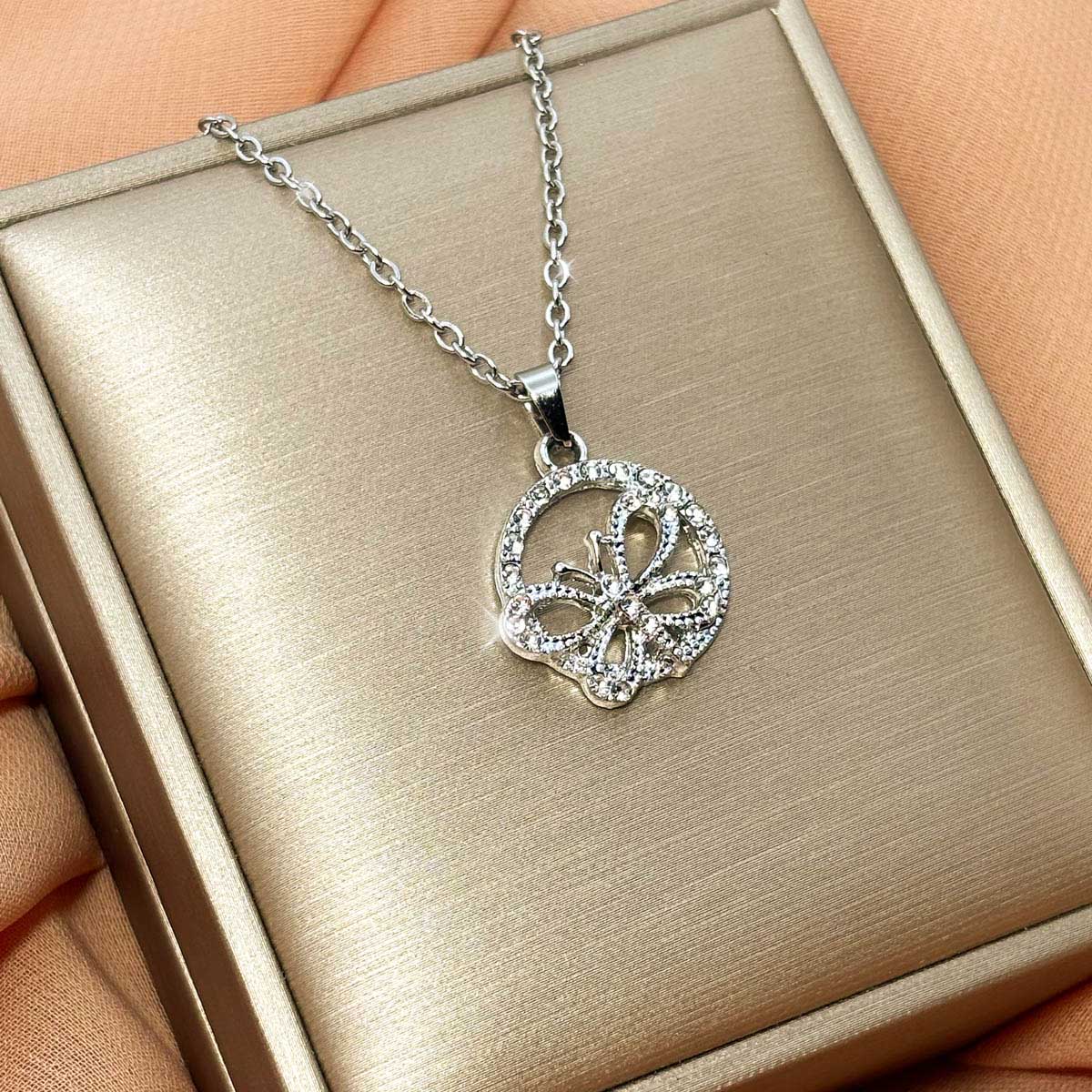 Silberfarbene Damen-Halskette aus Edelstahl mit einer runden, zirkoniabesetzten Plakette und integriertem Schmetterling-Motiv, Studioaufnahme.