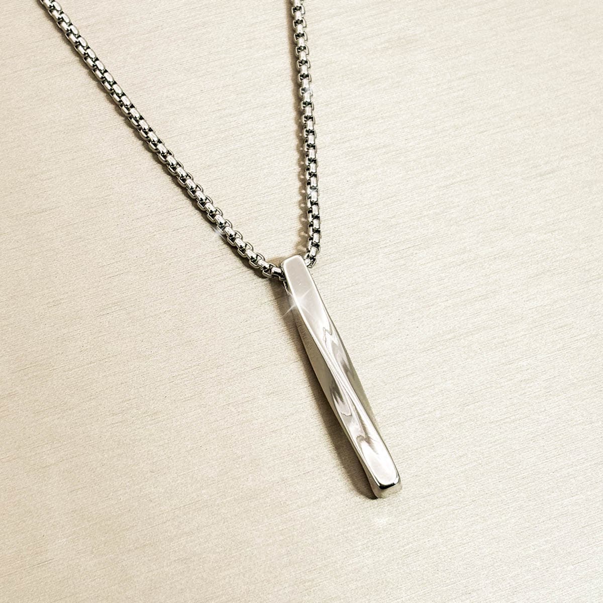 Silberfarbene Herren-Halskette mit schlichtem, gedrehtem Stab-Anhänger aus Edelstahl, Produktfoto von links.