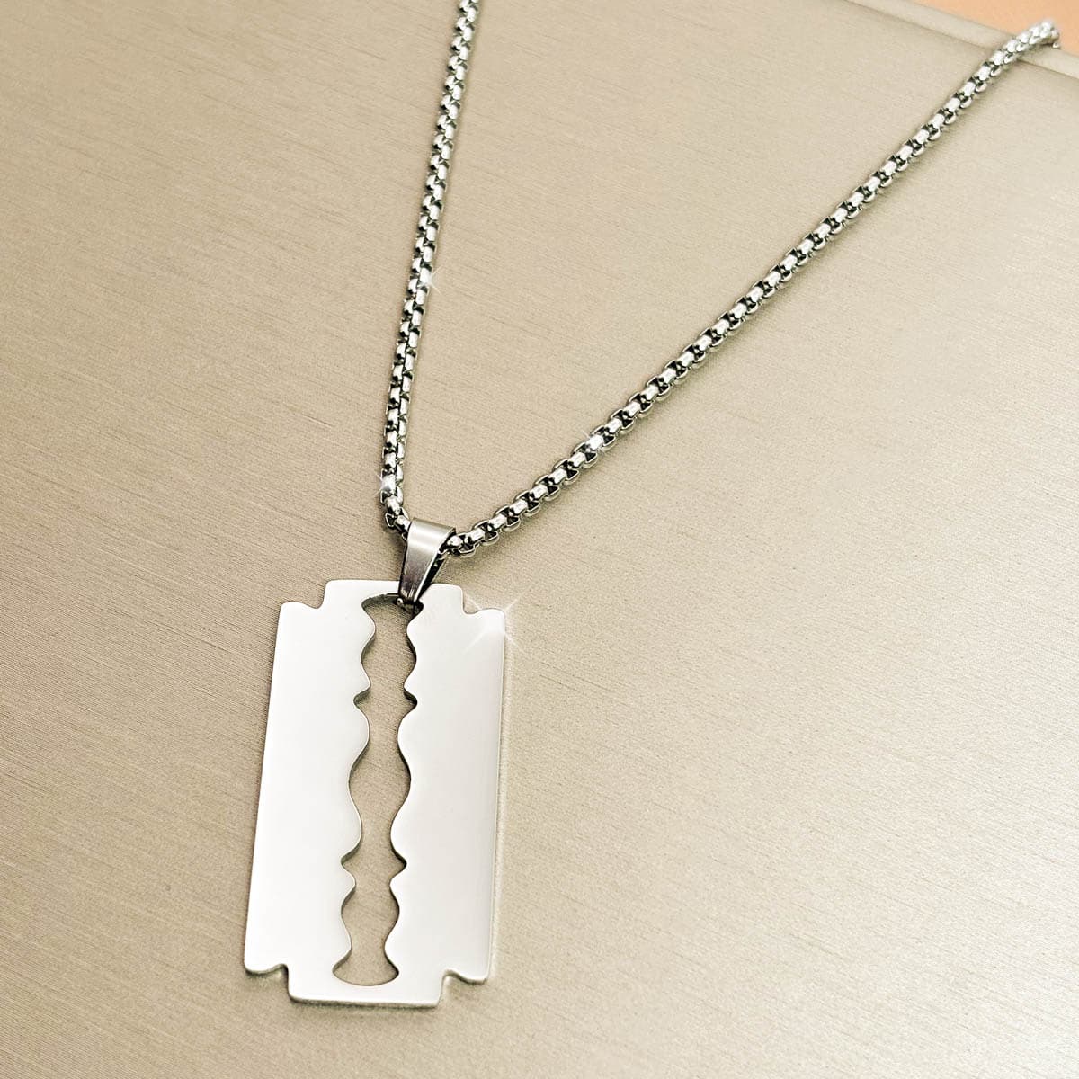 Edelstahl-Herrenkette in Silber mit glänzendem Anhänger in Form einer Rasierklinge, Nahaufnahme von links