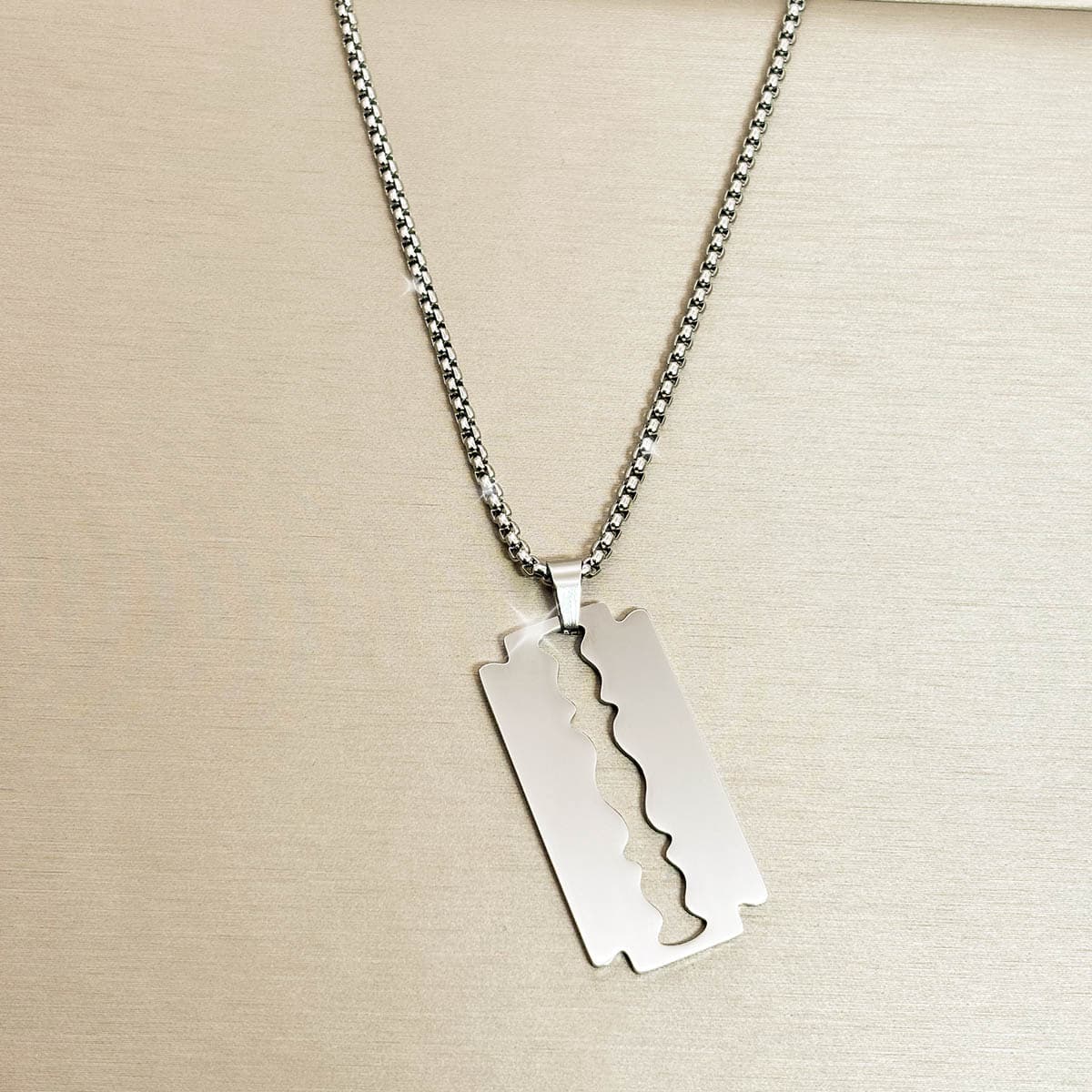 Edelstahl-Herrenkette in Silber mit glänzendem Anhänger in Form einer Rasierklinge, Nahaufnahme.