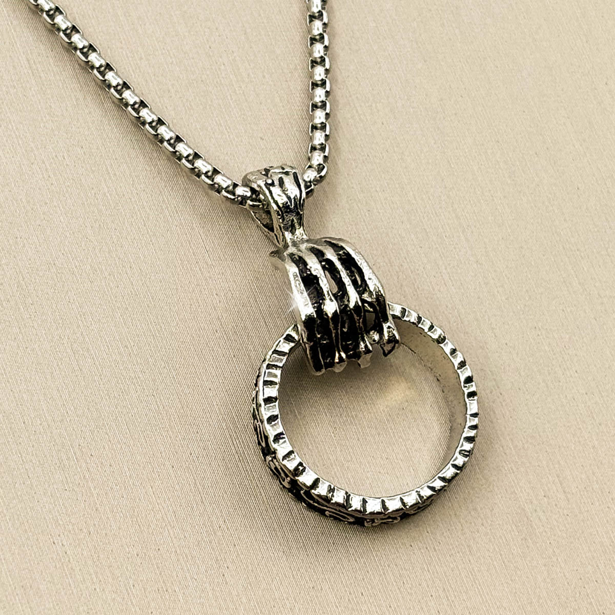 Silberfarbene Herren-Halskette aus Edelstahl mit einem strukturierten Ring-Anhänger, gehalten von einer steinernen Klaue, Vorderansicht.