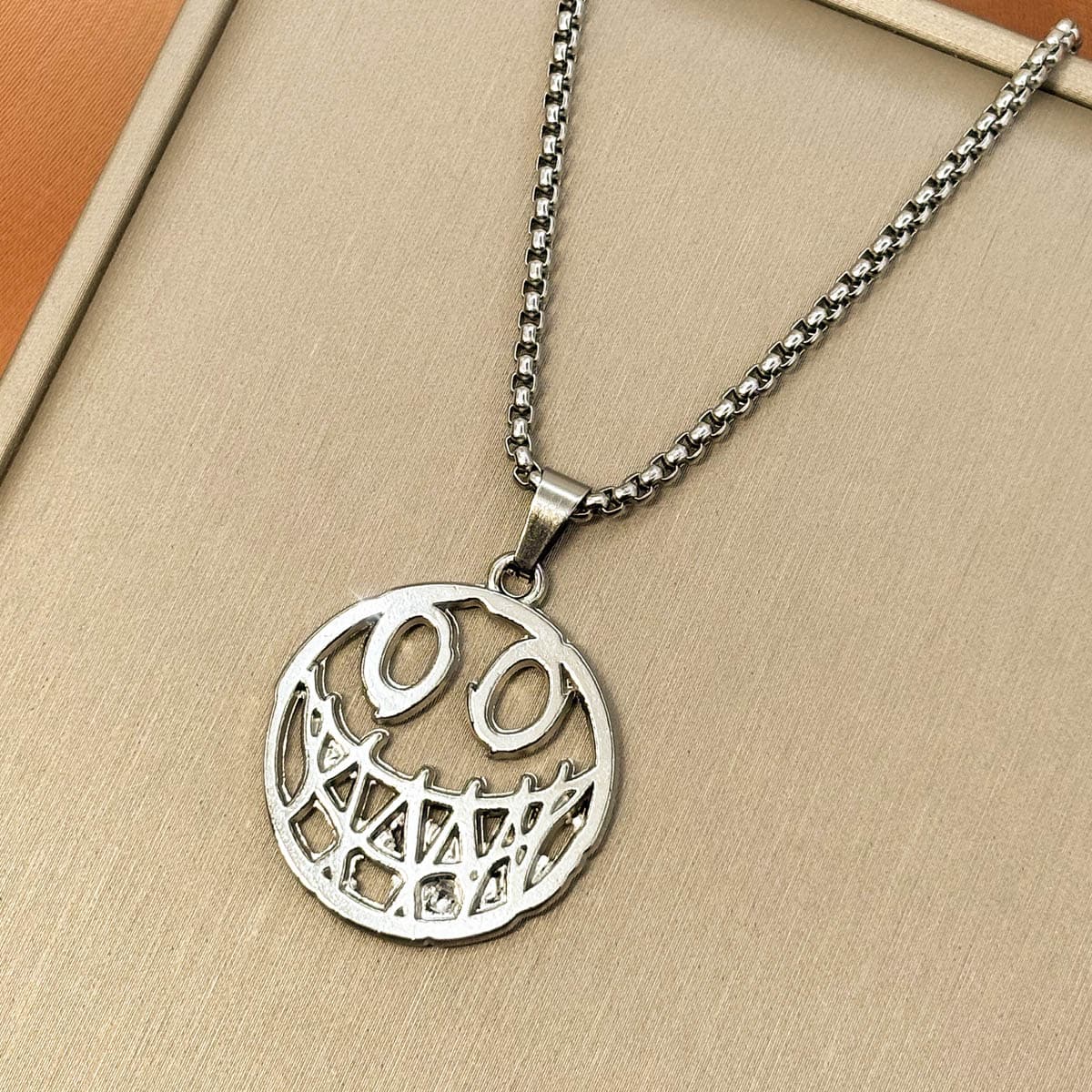 Herren-Halskette aus Edelstahl in Silber mit einem runden, grinsenden Smiley-Anhänger im Cut-Out-Design, Produktfoto von rechts.