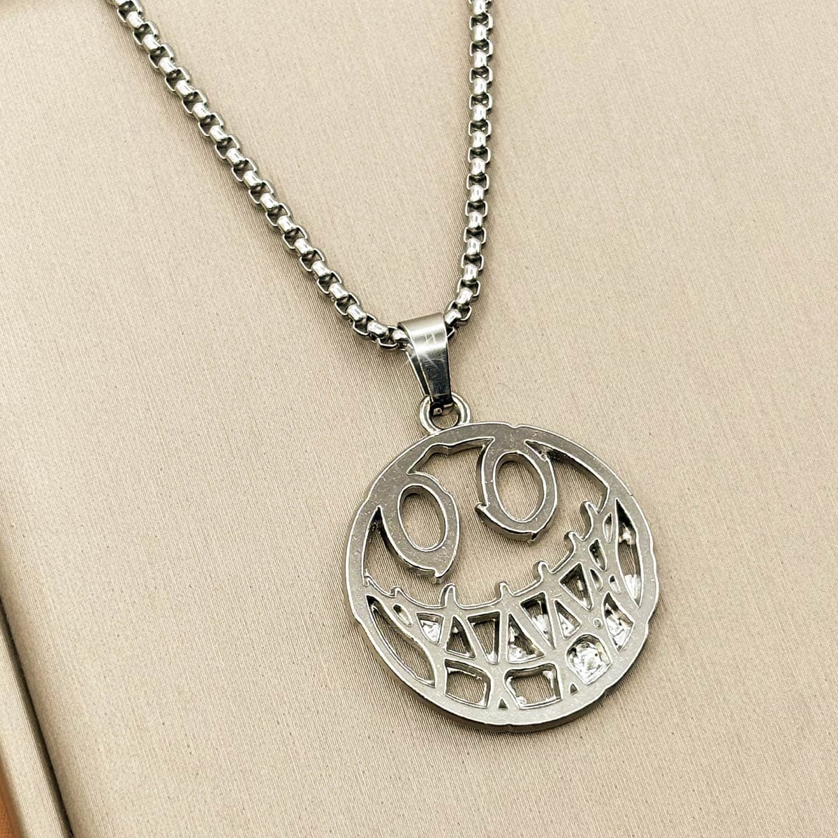 Herren-Halskette aus Edelstahl in Silber mit einem runden, grinsenden Smiley-Anhänger im Cut-Out-Design, Produktfoto von links.