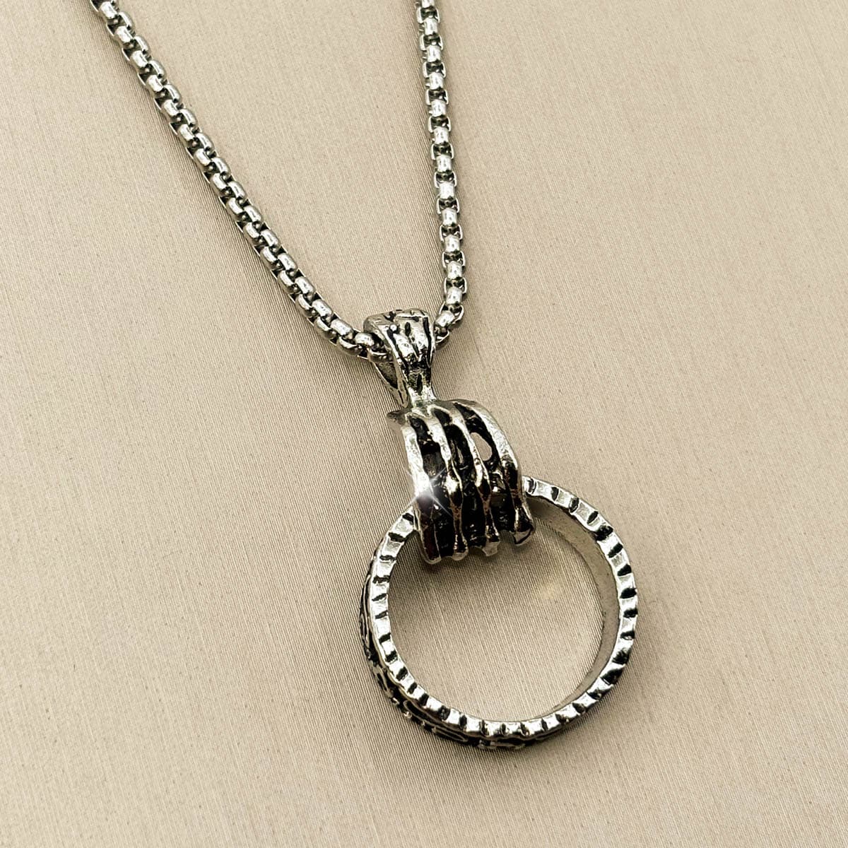 Silberfarbene Edelstahl-Herrenkette mit einem Anhänger in Form einer Hand, die einen strukturierten Ring greift, Studioaufnahme von links.