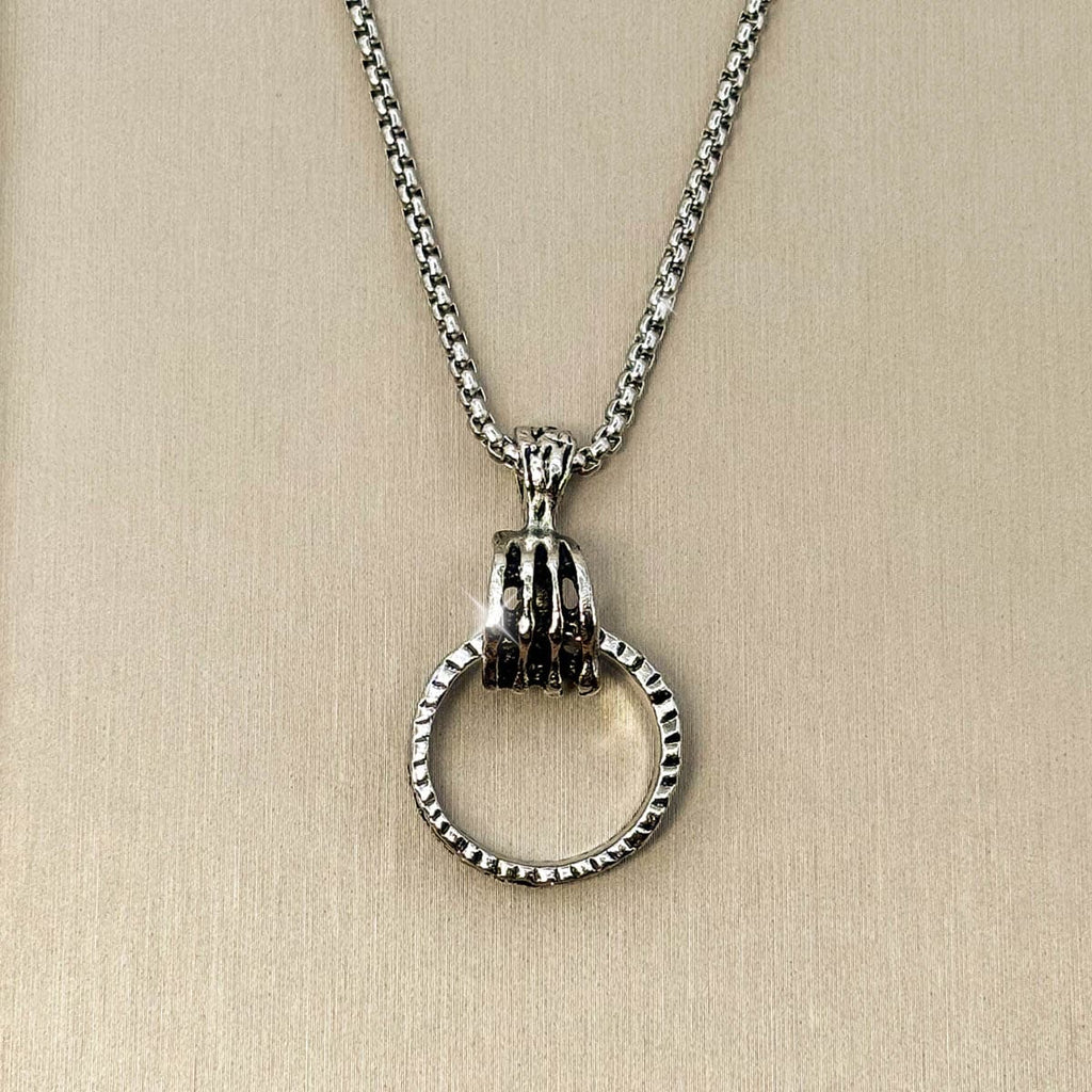 Silberfarbene Edelstahl-Herrenkette mit einem Anhänger in Form einer Hand, die einen strukturierten Ring greift, Detailaufnahme.