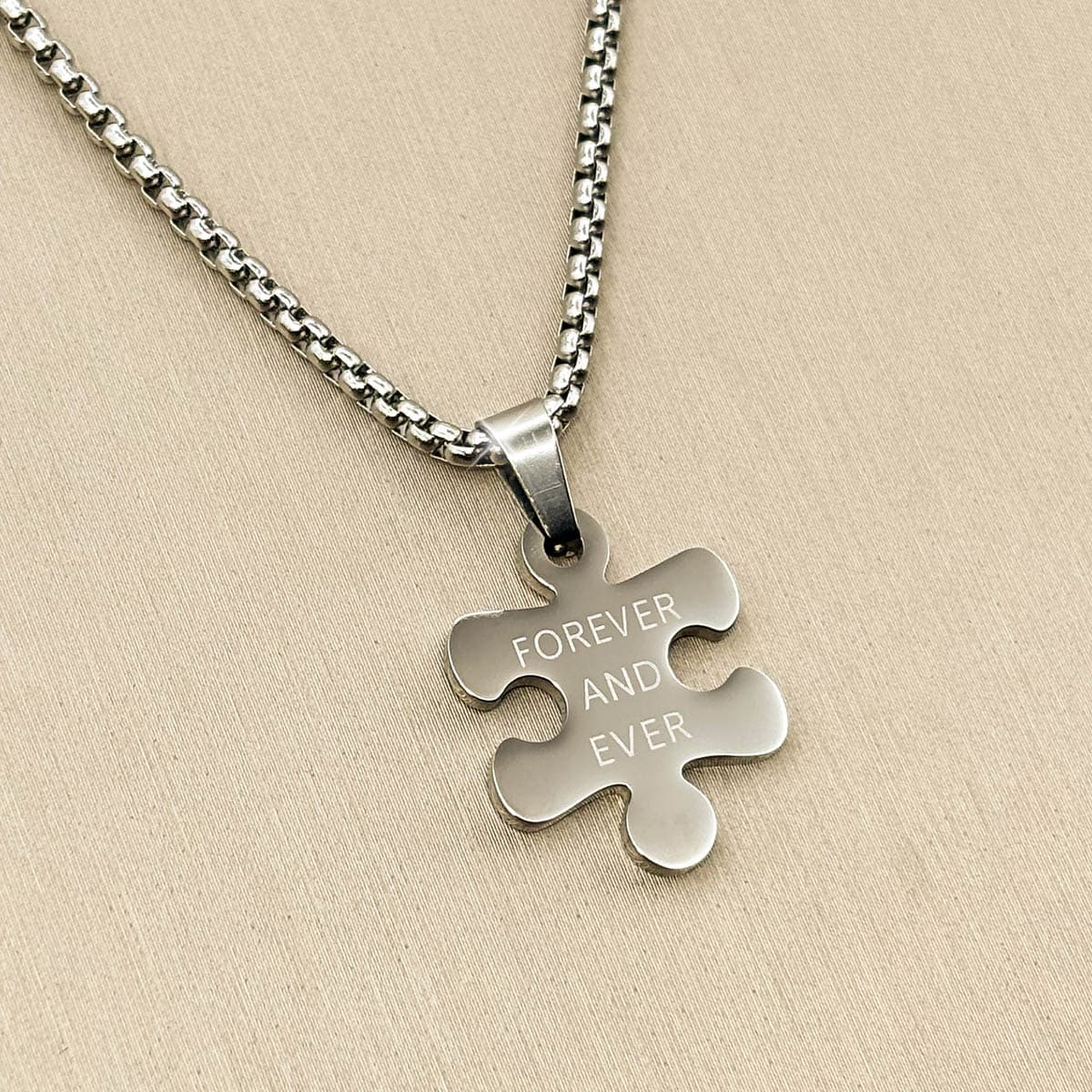 Herren-Halskette aus silberfarbenem Edelstahl mit einem gravierten Puzzleteil-Anhänger, Nahaufnahme von links.